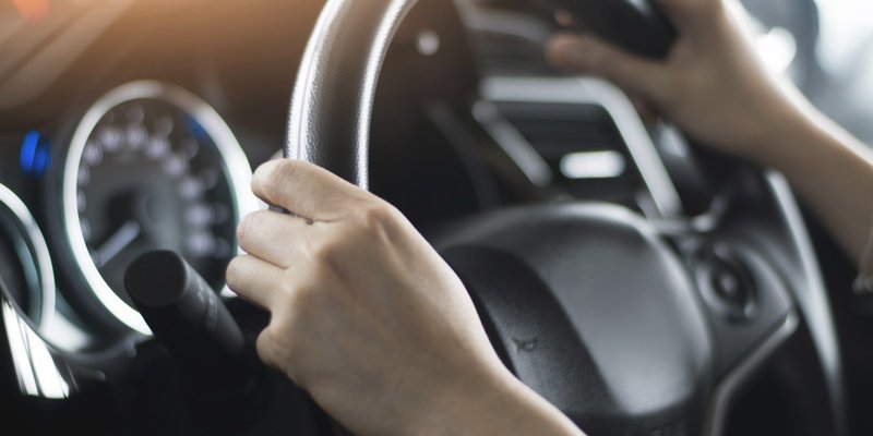 Two hands grip the steering wheel of a car